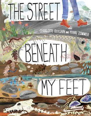The image shows the cover of the children’s book The Street Beneath My Feet by Charlotte Guillain and Yuval Zommer. The illustrated design depicts a cross-section of the ground under a street, showing layers of soil, rocks, roots, fossils, and bones beneath a person’s feet, visually exploring what lies underground in a colorful, educational style.
