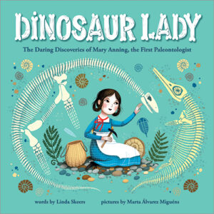 The image shows the cover of the children’s book “Dinosaur Lady: The Daring Discoveries of Mary Anning, the First Paleontologist.” It features an illustrated woman in a blue dress sitting among fossils and bones, using a small tool to examine one, surrounded by a circular arrangement of prehistoric skeletons and shells on a teal background.